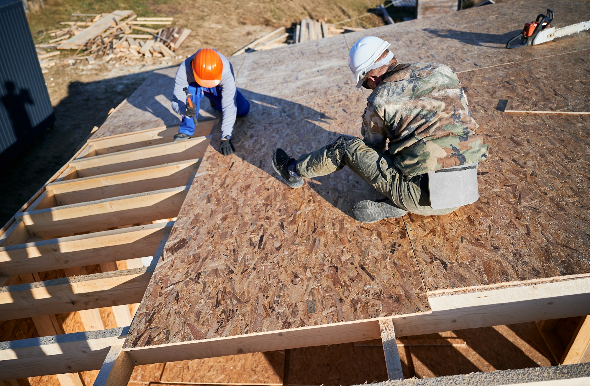 Carpenter hammering nail into OSB panel while building wooden frame house.